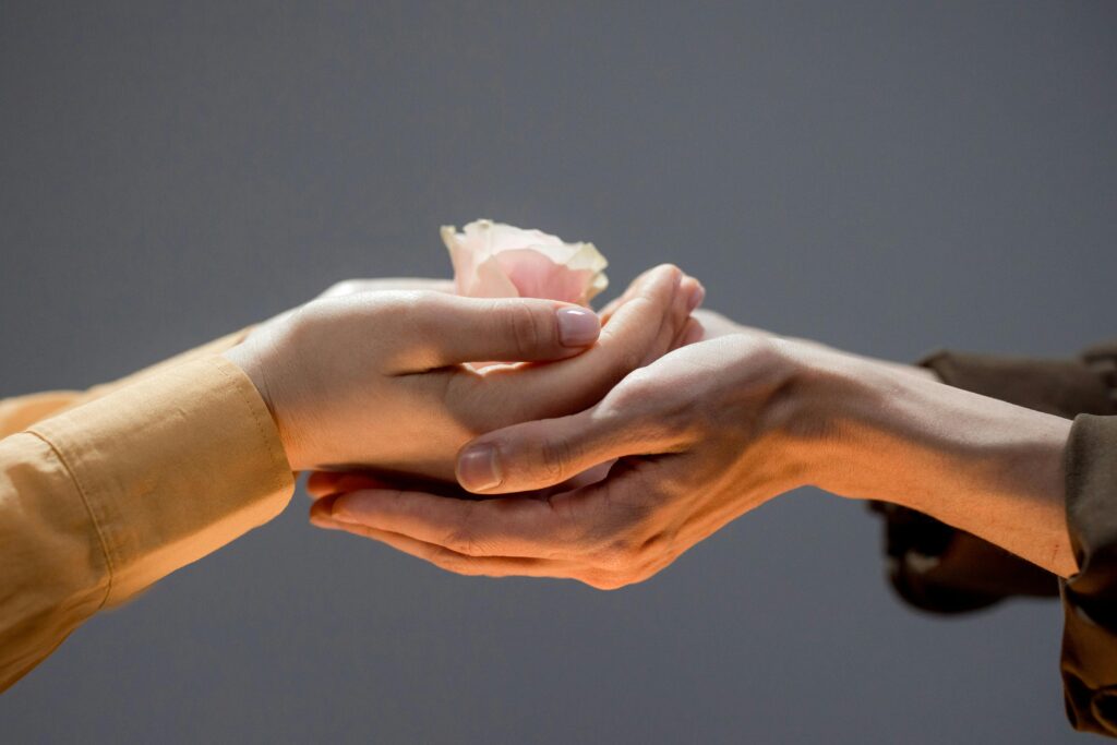 Close-up of hands exchanging a delicate rose, symbolizing care and connection.